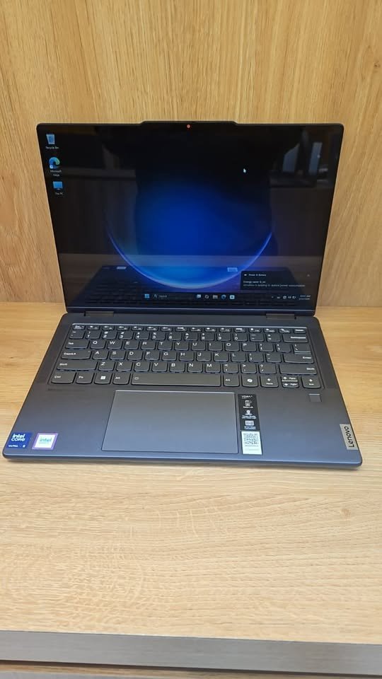 Lenovo Yoga 7 2-in-1 laptop open front view featuring a full-size backlit keyboard, precision trackpad, Intel Core Ultra processor badge, and Windows 11 boot screen on display — dark gray chassis